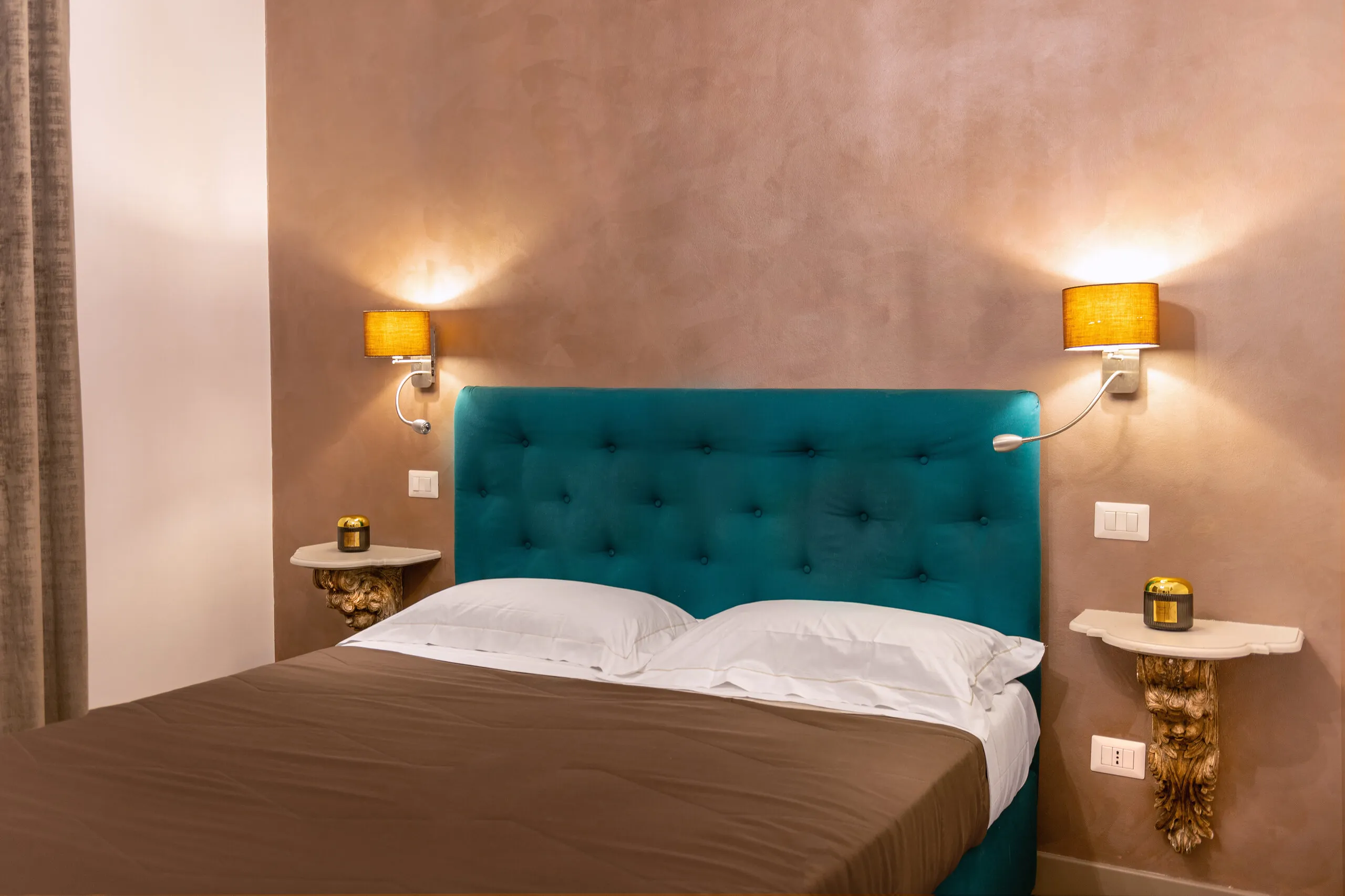 Il letto della Standard 01 visto di tre quarti, con copriletto marrone e mensole a cartiglio